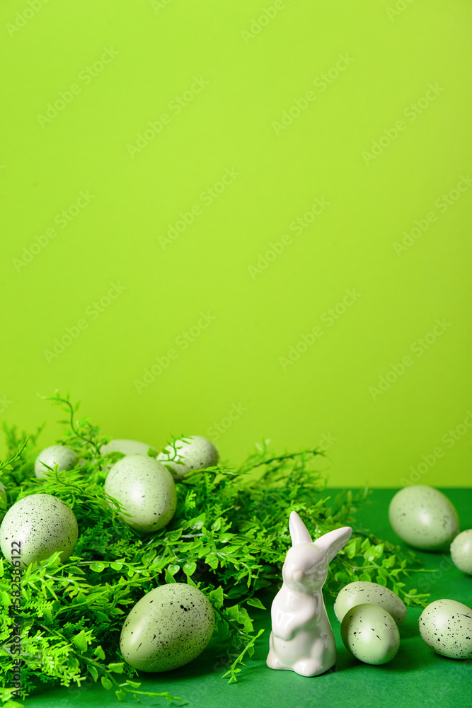 Easter eggs, porcelain bunny and plant leaves on green background