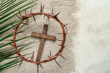 Wooden Cross With Crown Of Thorns And Palm Leaf On Sand. Good Friday Concept