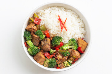 Stir fried chicken and broccoli bell pepper has rice in bowl on white wood table.