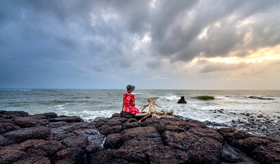 Wall Mural - A woman sitting on a rock watching the sunrise in  