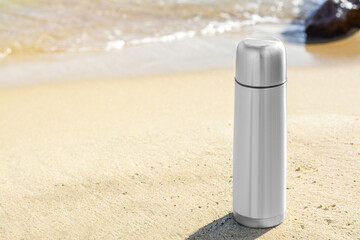 Wall Mural - Metallic thermos with hot drink on sandy beach near sea, space for text