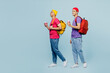 © ViDi Studio - Full body young students couple two friends men wearing casual clothes backpack bag together holding notebooks drink coffee isolated on plain pastel light blue background. High school college concept.