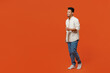 © ViDi Studio - Full body smiling happy fun cheerful cool young man of African American ethnicity wearing light shirt casual clothes walking going isolated on orange red background studio portrait. Lifestyle concept.