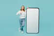 © ViDi Studio - Full body young woman wear striped hoody point finger on big huge blank screen mobile cell phone smartphone with workspace copy space mockup area isolated on plain pastel light blue cyan background.