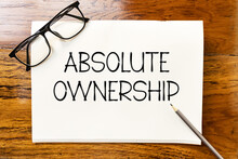 Absolute Ownership Text On Blank Notebook Paper On Wooden Table With Pencil And Glasses Aside. Business Concept And Legal Concept About Absolute Ownership.