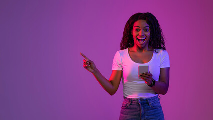 Poster - Black Female In Neon Light Holding Smartphone And Pointing At Copy Space