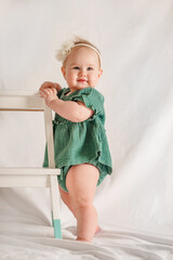 Wall Mural - Portrait of a beautiful Caucasian baby toddler girl with a bow and muslin dress on a white background