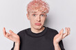 Hesitant pink haired guy shrugs shoulders feels uncertain looks confusingly at camera purses lips dressed in casual black t shirt doesnt know right answer isolated over white background. So what