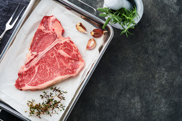 Wall Mural - Thick Raw T-Bone Steak. Dry-aged Raw T-bone or porterhouse beef meat Steak on parchment paperwith herbs and salt on dark background. Top view and copy space.