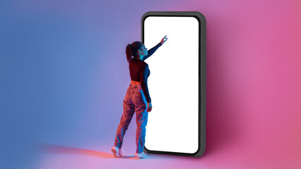 Poster - Full length shot of black lady touching screen of huge smartphone in neon light, mockup for app or website design