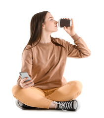 Poster - Pretty young woman with smartphone drinking coffee while sitting against white background