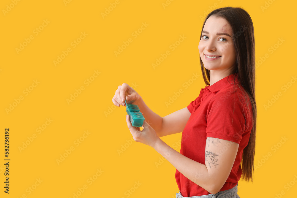Young woman with container of vitamin supplements on yellow background