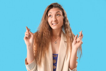 Sticker - Beautiful young woman in jacket crossing fingers on blue background