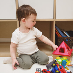 Wall Mural - Toddler baby boy is playing with a sorter puzzle on a rug in the nursery. A small child is playing with toys. Kid aged one year eight months