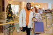 © Roman - Discount Prices. Smiling awesome couple enjoys shopping In Mall Together red-haired girl with coffee looking At her boyfriend with couple Walking In Store With Bright Shopper Bags Seasonal Sales