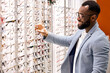 © Roman - Handsome young smiling bearded african man buying eyeglasses at optics . Consumerism, shopping, lifestyle, medicine concept, close up side view shot, happiness.
