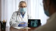 © Robert Peak - Woman doctor wearing gloves and face mask shares her tablet computer screen with patient and shows x-ray. Concept of medical visit during pandemic.