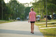 Back view of sad young child girl walking alone along the green street on sunny summer day