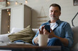 © opolja - Happy smiling senior man using smartphone device while sitting on sofa at home