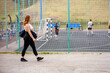 © metelevan - a girl with red hair walks with a bag on her shoulder past the sports ground on a summer evening
