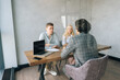 © dikushin - Remote view from glass of three businesspeople in formal wear negotiating brainstorming sitting at boardroom. Back view of male and female partners listening unrecognizable manager presenting project.