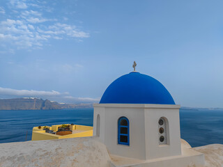 white church dome with blue roof in oia, santorini island with a sea view in background