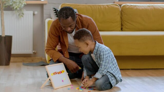 Wall Mural - Early kids development. Caring black dad teaching his little son alphabet, cute boy putting magnetic letters on board