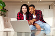 © Богдан Маліцький - young multiracial couple sitting on comfortable sofa and looking into laptop at home