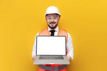 asian foreman in uniform showing blank laptop screen on yellow isolated background, korean civil engineer in hardhat