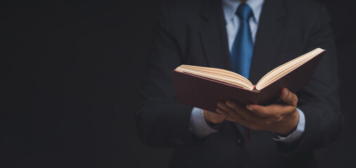 businessman in a suit reading a book while standing on a black background