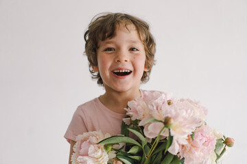 Cheerful happy child with Peonys bouquet. Smiling little boy on white background. Mother's Day. Love and romantic concept