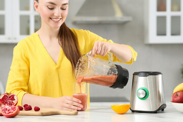 Wall Mural - Woman pouring tasty smoothie into glass at white table in kitchen