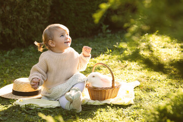 Wall Mural - Happy little girl with cute rabbit on green grass outdoors