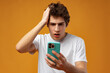 © fotofabrika - Photo of young guy holding telephone reading bad news on yellow background