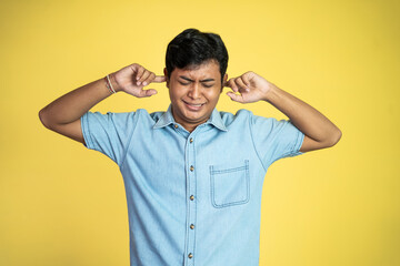 young Asian man serious covering ears with two hands in an isolated background