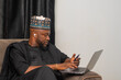 © WISDOM - young african businessman seated using his mobile phone and working on his laptop