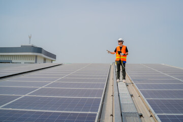 Asian engineer wearing protective vest and white hardhat standing pointing to the copy space on solar panels roof while holding tablet with blue sky background, Photovoltaic technology concept.