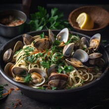 A Front View Of A Black Metal Bowl With Linguine Alle Vongole. The Pasta Is Cooked With Clams, Garlic, White Wine And Parsley. The Clams Are Open And Juicy. The Bowl Is Placed On A Dark Slate Board.