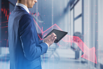 Poster - Close up of businessman hands using tablet with red candlestick arrow going down on blurry office interior background. Economic recession and crisis concept. Double exposure.