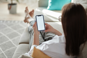 mock up white screen blank mobile phone in woman hands holding lying on the sofa back view