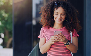 Canvas Print - Im making my way over there soon. a young woman using her cellphone while walking through the city.