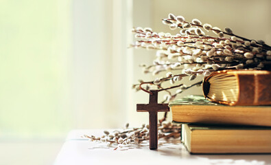 wooden cross, old biblical books and willow twigs close up on table, abstract light background. orth