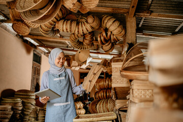 Wall Mural - asian muslim woman at her traditional bamboo products shop holding tablet pc