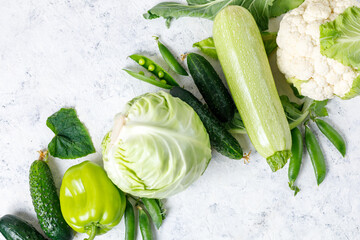 Wall Mural - Border of organic green raw vegetables on white table. Top view of healthy organic food. Copy space