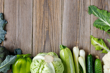Wall Mural - Border of green raw vegetables on wooden background. Top view of healthy organic food. Copy space