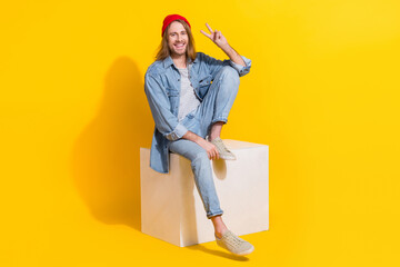 Sticker - Full length photo of cute attractive man wear denim jacket sitting showing v-sign space isolated yellow color background