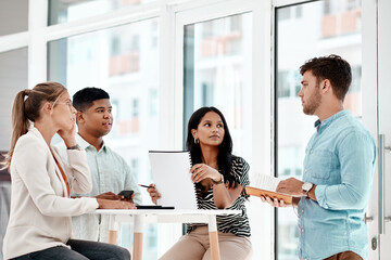 Poster - Hes got a few ideas. a group of young business colleagues gathered around a table in their office.