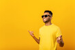 Excited positive young arab man in sunglasses rejoicing, raising hands up and having fun, having good summer mood. Indoor studio shot isolated on yellow background