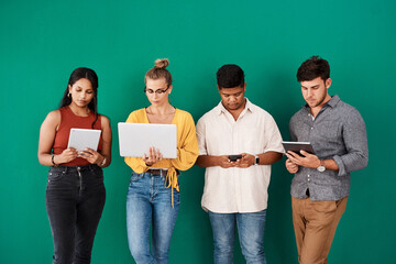 Poster - Staying connected to their online and mobile channels. a group of young designers using digital devices while standing together against a green background.