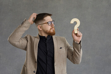 i don't understand. serious puzzled young man in suit and geek hipster glasses holding question mark